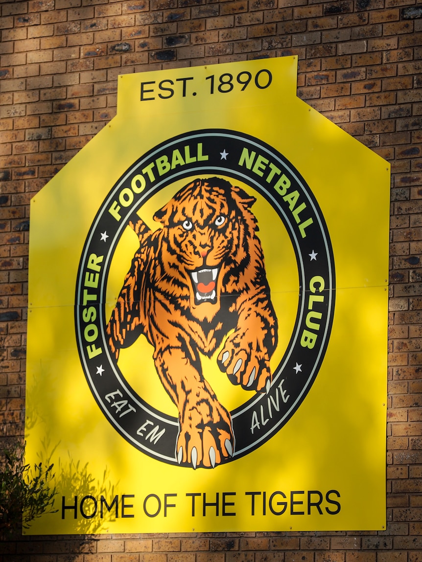 Dappled light hits a yellow sign on a brick wall of the Foster Football and Netball Club 