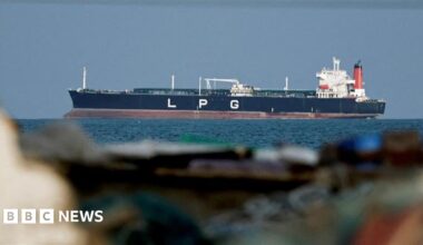 Close up of a ship on blue water in the background. In the foreground are rocks