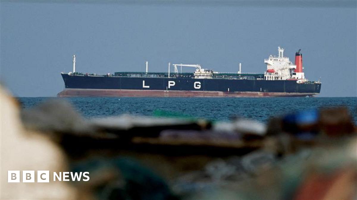 Close up of a ship on blue water in the background. In the foreground are rocks