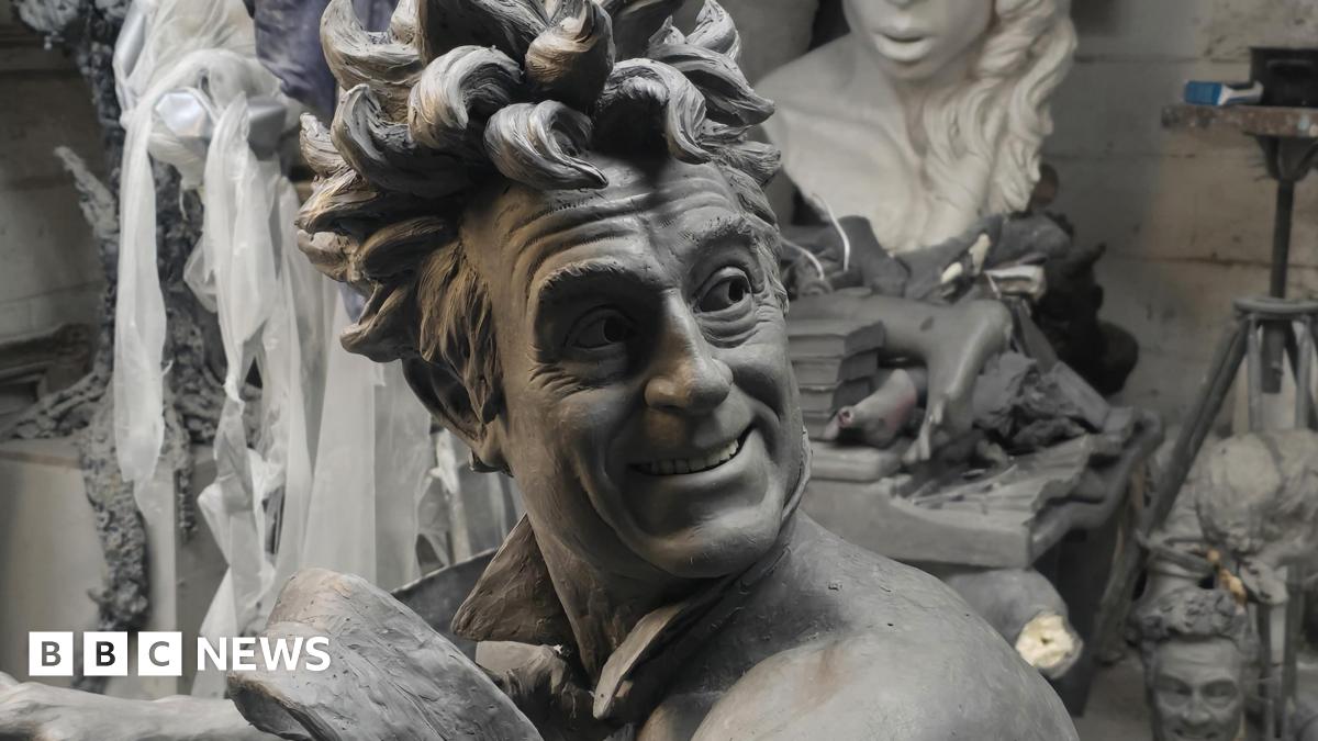 A close up picture of the clay model used for the sculpture showing Terry Jones with wild hair and smiling. He wears only a tie that looks like it is blowing in the wind
