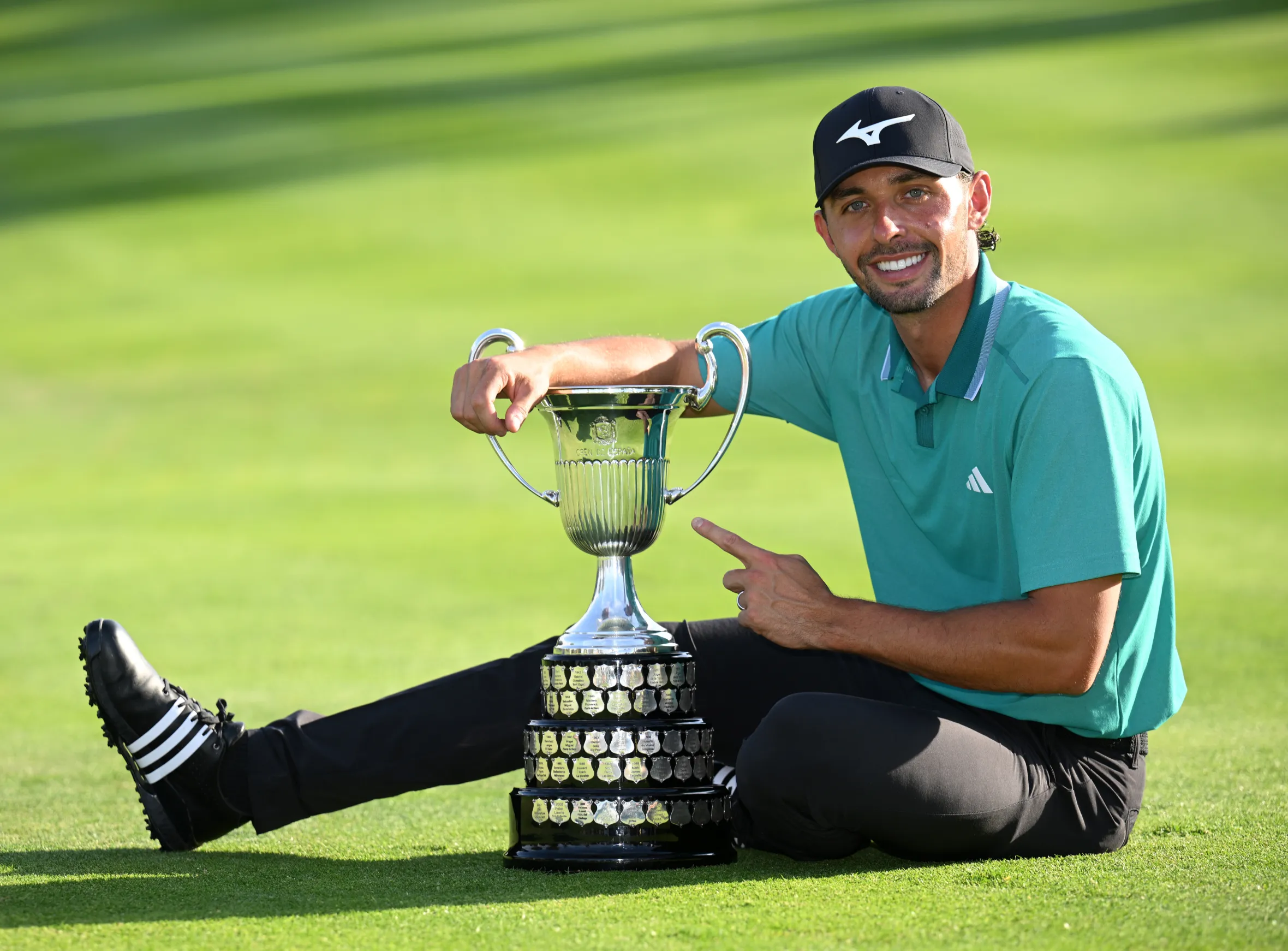 Marco Penge sits on the grass next to the Open de España trophy.