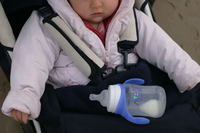 A baby in her buggy with an empty baby milk bottle, Northumbria, UK.