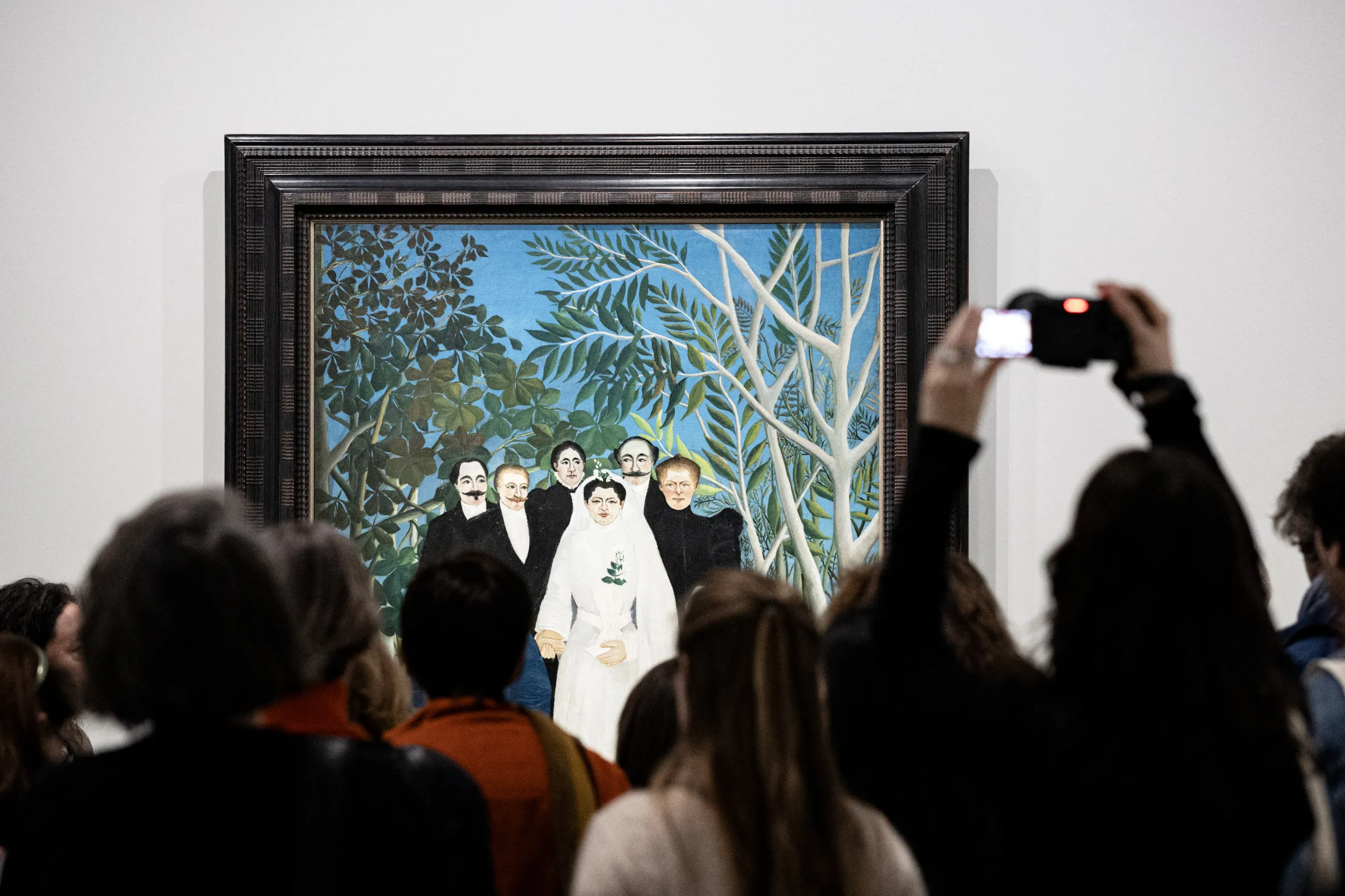 Visitors at an exhibition looking at Henri Rousseau's "The Wedding" painting.