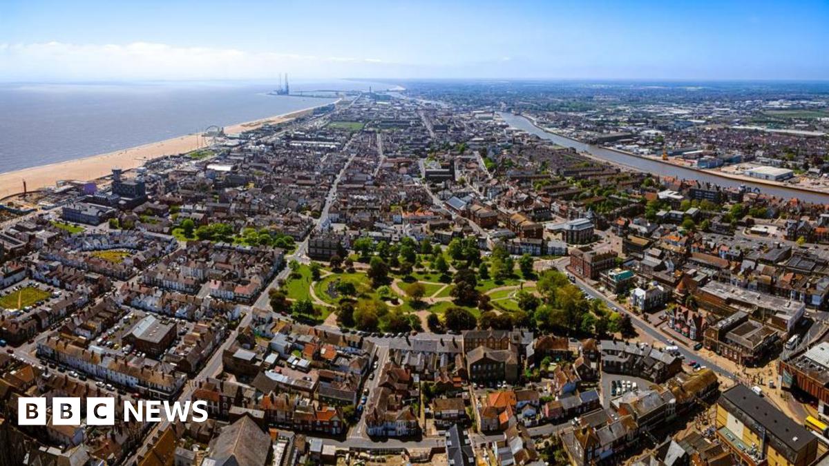 A bird's eye view of Great Yarmouth which includes areas of dense housing and a park, with the beach and the sea to the left. It is a sunny day and the sky is blue.