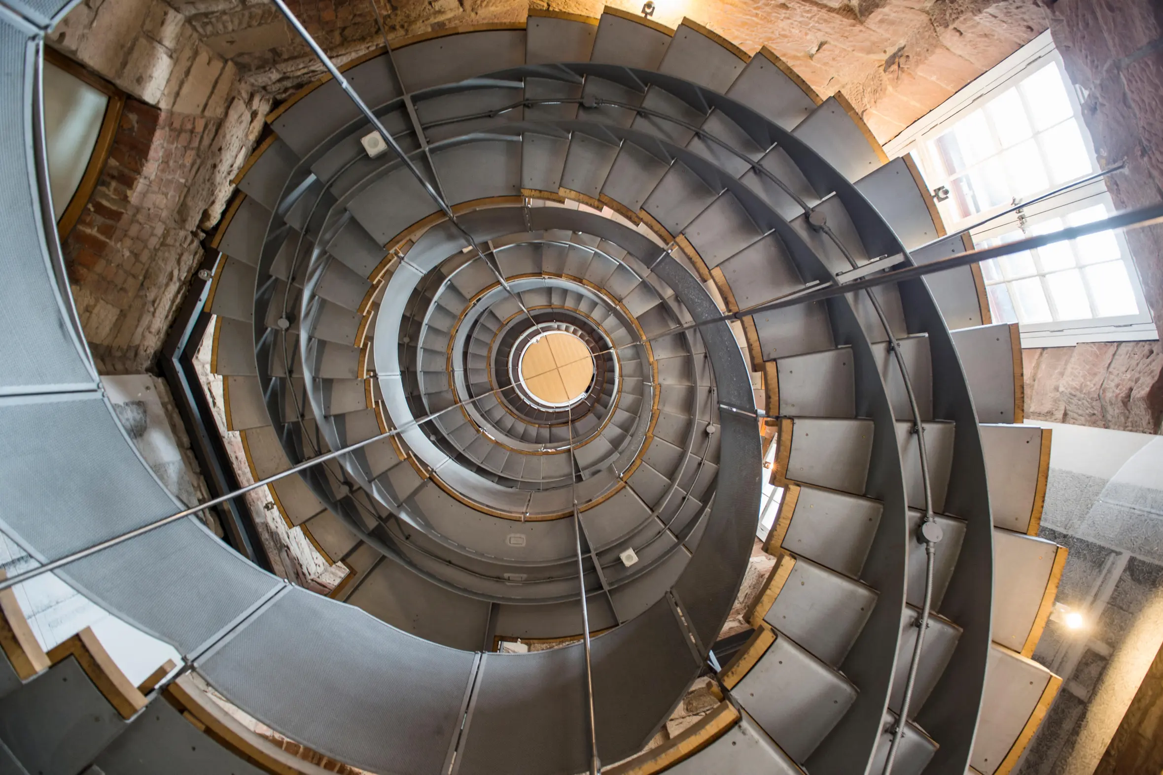 A low-angle view looking up a metal spiral staircase within The Lighthouse Cultural Center in Glasgow, Scotland.