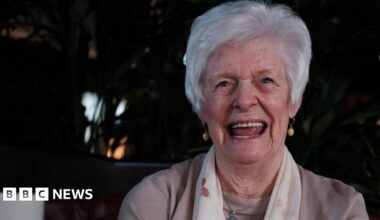 Marie McLaren smiles for the camera. She has short grey hair and is wearing a white scarf.