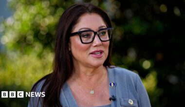 Lori Chavez-Deremer in grey sweater, gold necklace, and black glasses