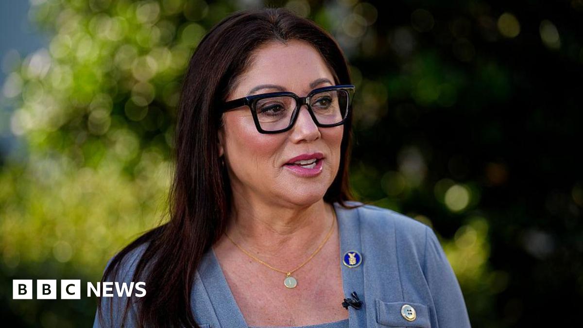 Lori Chavez-Deremer in grey sweater, gold necklace, and black glasses