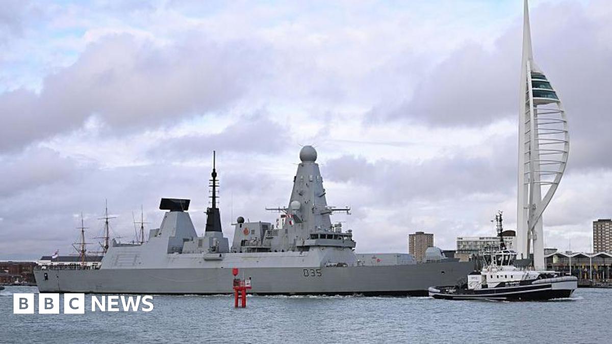 HMS Dragon, a large grey destroyer ship, sits on the water in Portsmouth Harbour, under a cloudy sky.