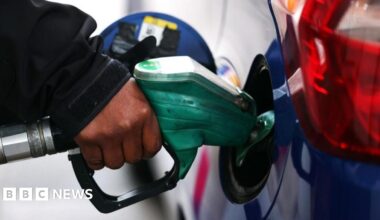 A close up of someone's hand on the pump while they fill their blue car with petrol