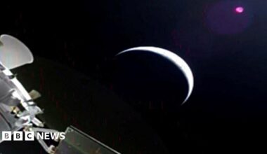 A slightly grainy image from Orion showing a planet - perhaps the moon, as a sliver with most of it in darkness, and part of Orion in the corner.