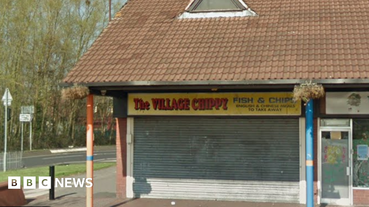 General view of the Village Chippy. It is a unit on a small parade of shops. Its shutters are down in the image.