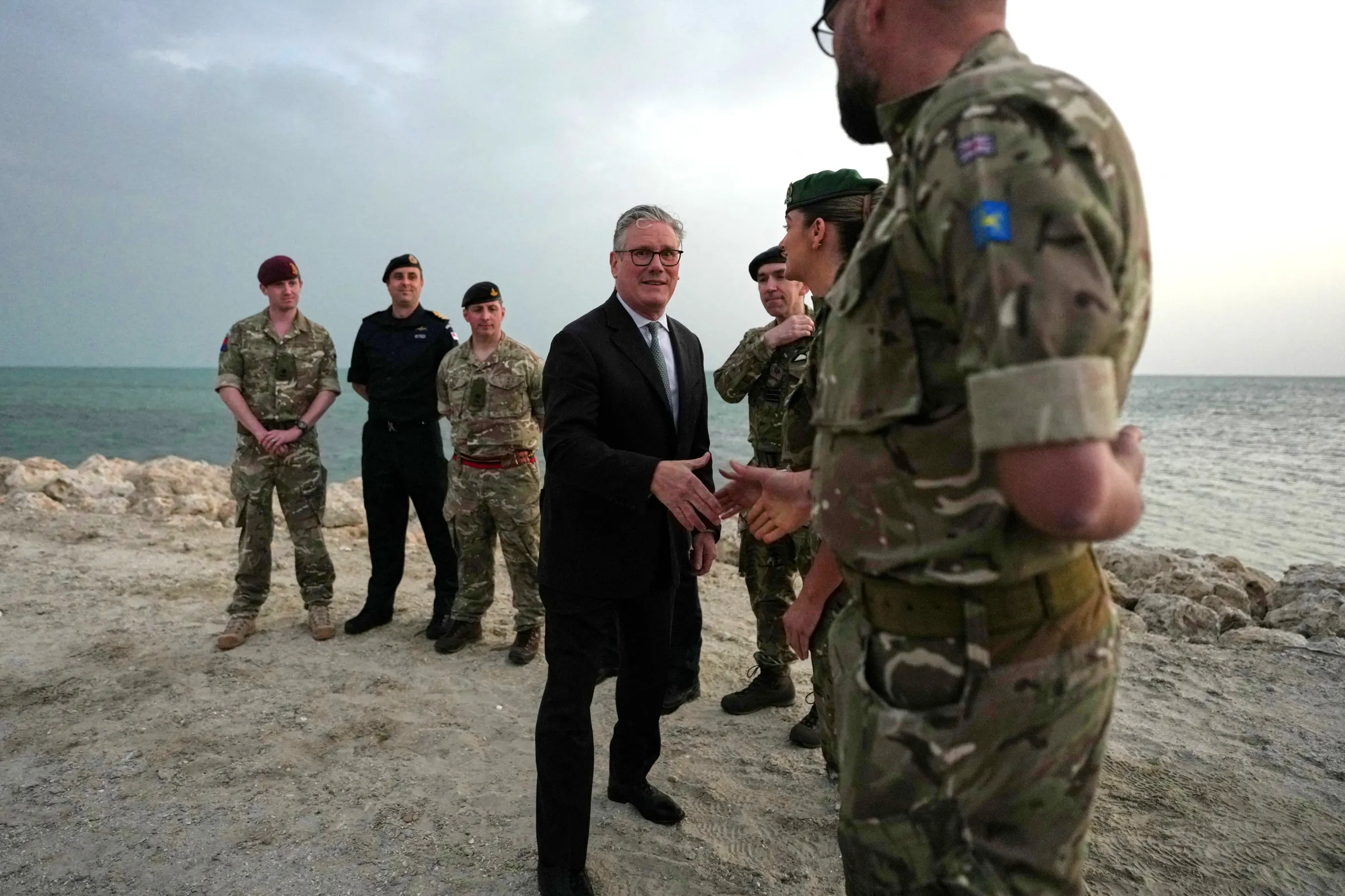Britain's Prime Minister Keir Starmer shaking hands with military personnel on a beach in Bahrain.
