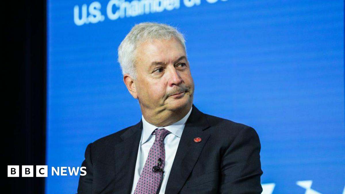 An image of Michael Rousseau sitting looking in the direction of his left. He is wearing a black suit jacket with an Air Canada logo pin, a white shirt and a patterned mauve tie. He has short grey hair.