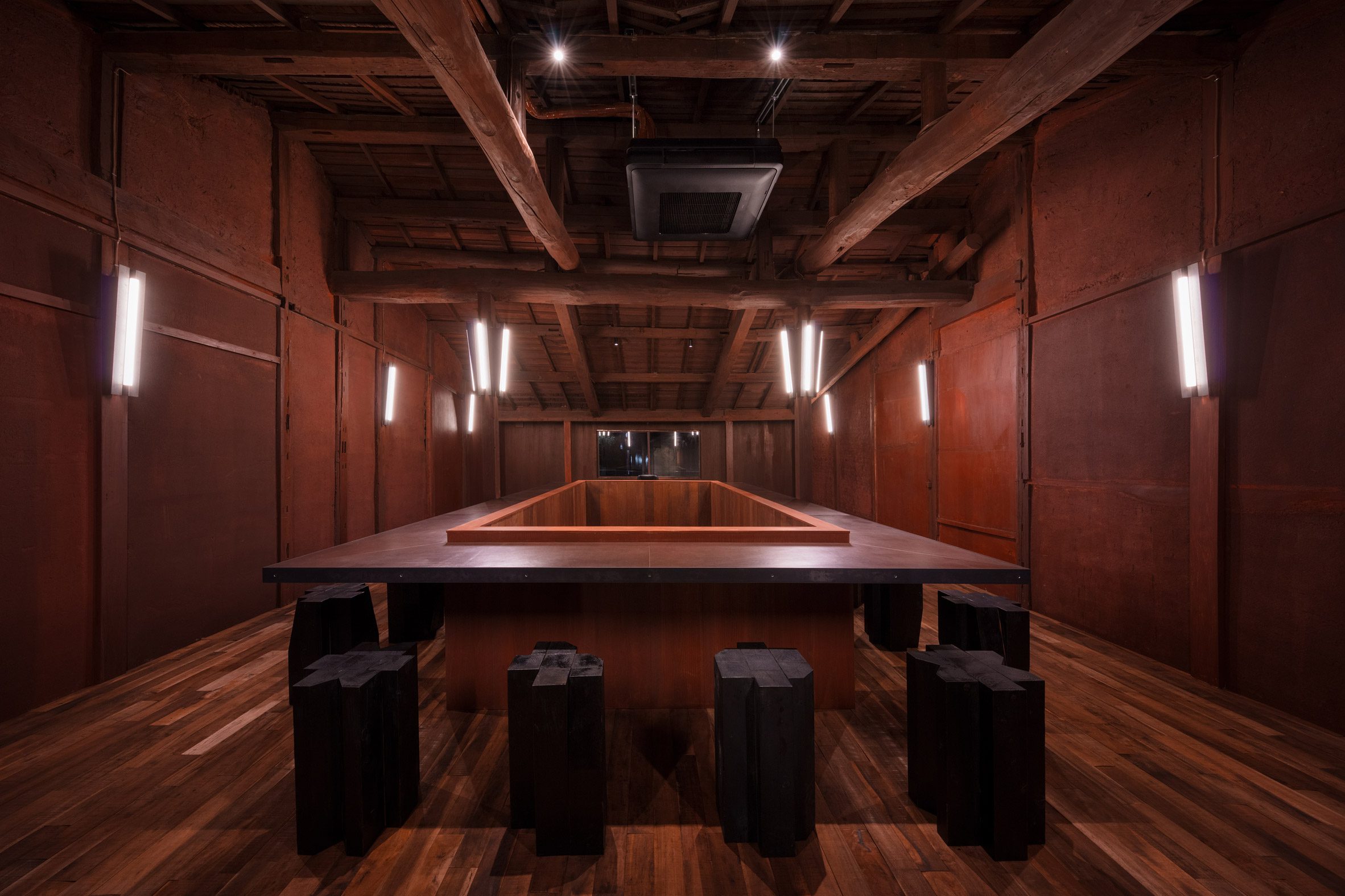 A terracotta-tinted cafe and bar with large, poligonal tiles on the floor, neon lights and sconces, wooden beams and furniture, and a dimly lit ambiance.