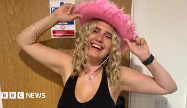 Phoebe is sat in a hosptial bed whilst undergoing a diagnostic test. She is smiling with serval medical wires attached to her head which has been shaved.