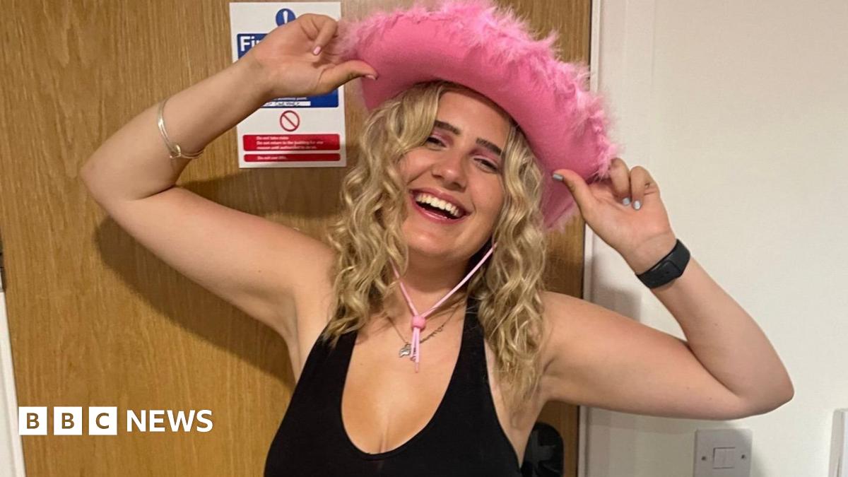 Phoebe is sat in a hosptial bed whilst undergoing a diagnostic test. She is smiling with serval medical wires attached to her head which has been shaved.