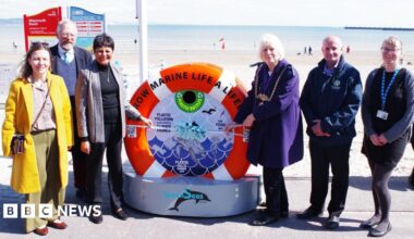 A group of six people standing either side of an installation shaped like a lifebuoy as they unveil the new unit