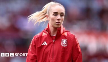 Missy Bo Kearns wearing a red jacket with an Aston Villa badge on the chest