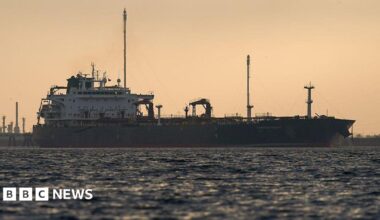 An oil tanker at sea silhouetted against a sky at sunset.