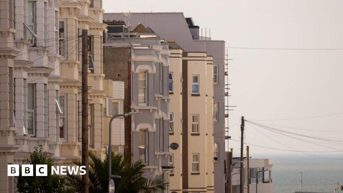 A row of light-coloured terraced buildings on a clear day. The sea can be seen in the background.