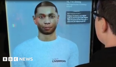 A digital depiction of a young man wearing a white top with the Visit Liverpool logo on a large screen with some text captions in the top right corner. A man with glasses can be seen on the right using the service on screen.