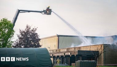 Firefighters using crane at RAF Fairford. They are spraying water onto a building and there is a green tent in the front of the image.