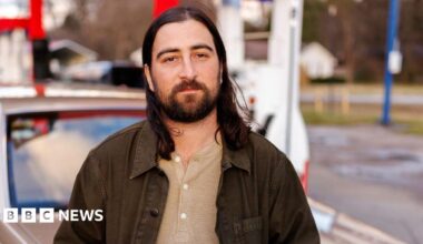 Noah Kahan leans against a vintage station wagon, in a promotional photo for his single The Great Divide.