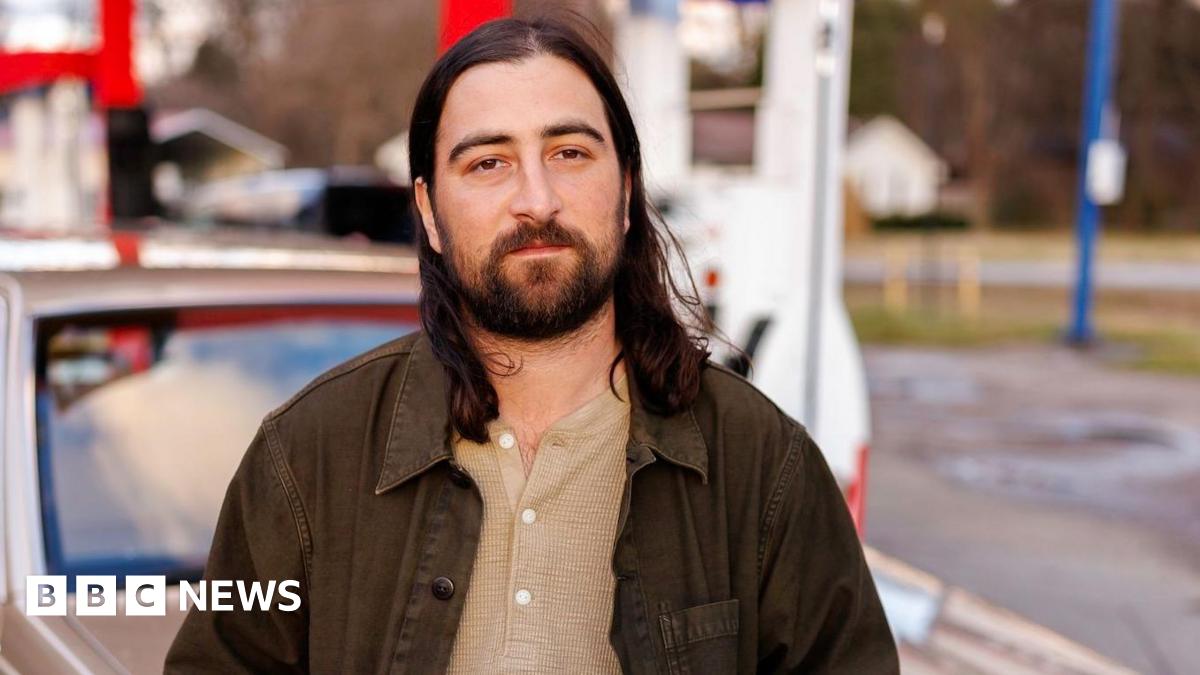 Noah Kahan leans against a vintage station wagon, in a promotional photo for his single The Great Divide.