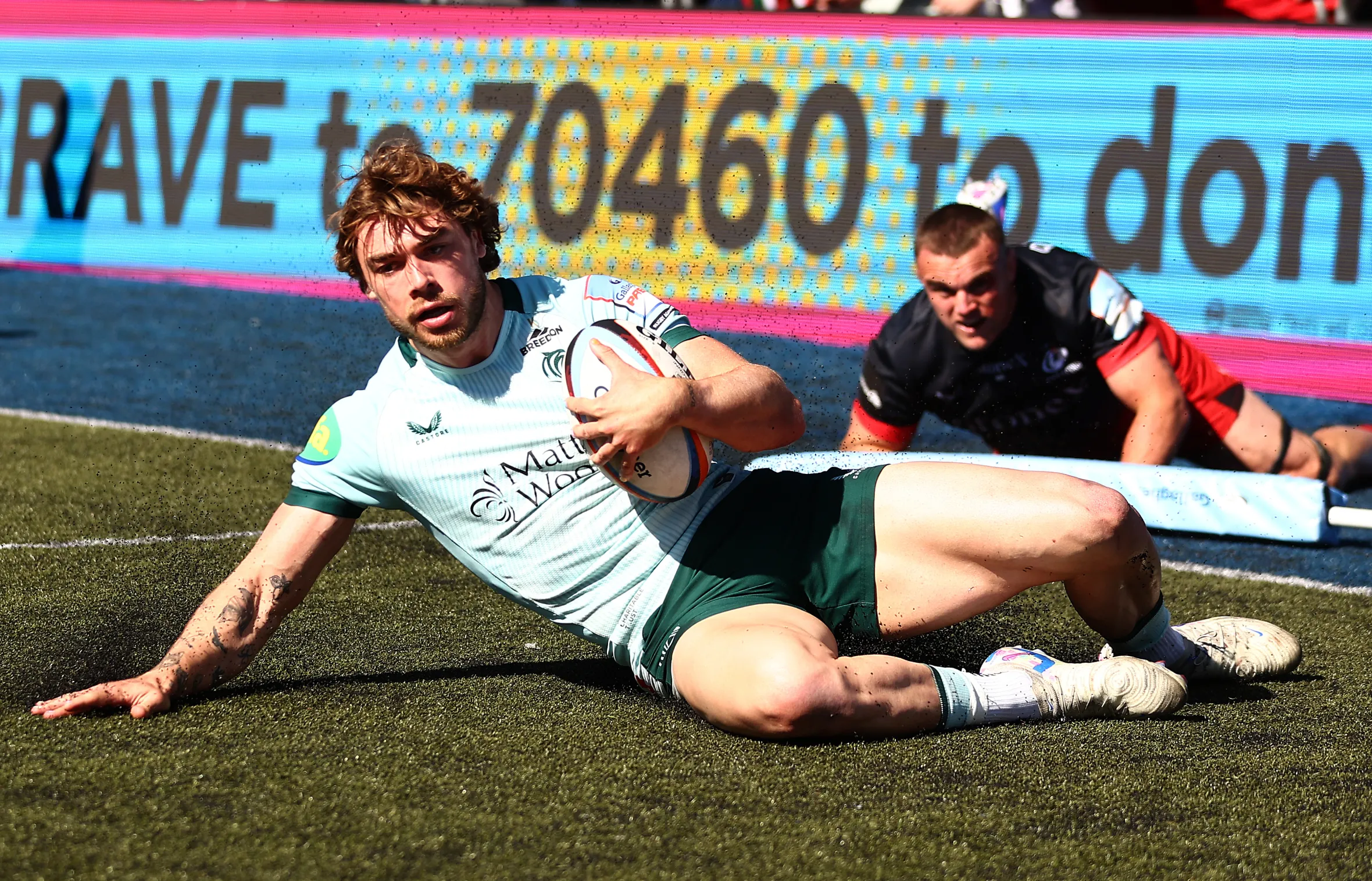 Ollie Hassell-Collins of Leicester Tigers scores a try while a Saracens opponent attempts to tackle him during a rugby match.