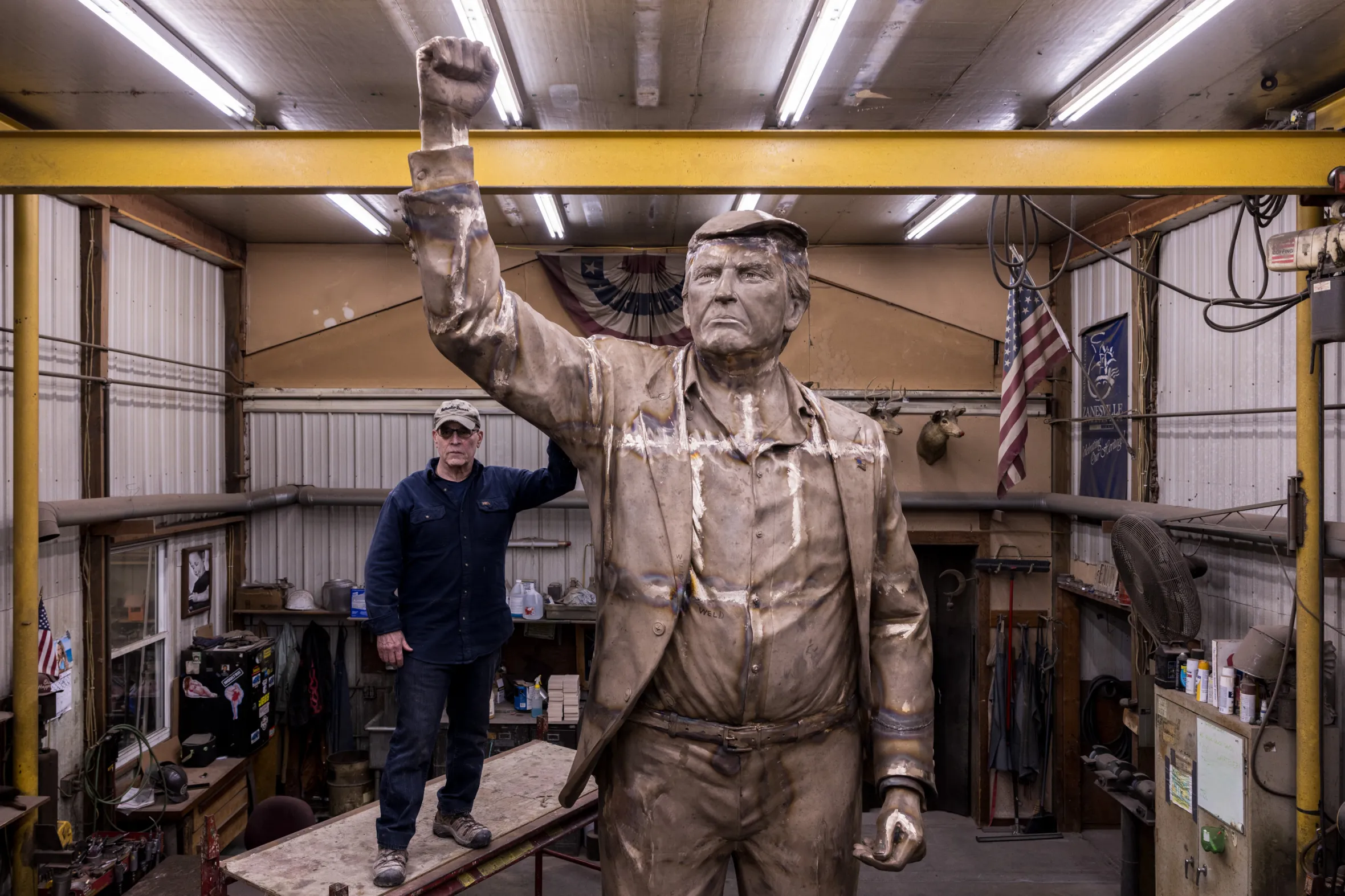 Alan Cottrill posing next to his large, bronze sculpture of a man.