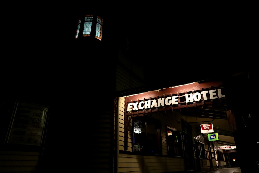Exterior of a pub at night time with the words Exchange Hotel illuminated and a high window dimly light at top of building