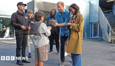 A small boy faces the Duke and Duchess of Sussex, as Prince Harry holds a fur ball and others surround them watching on.