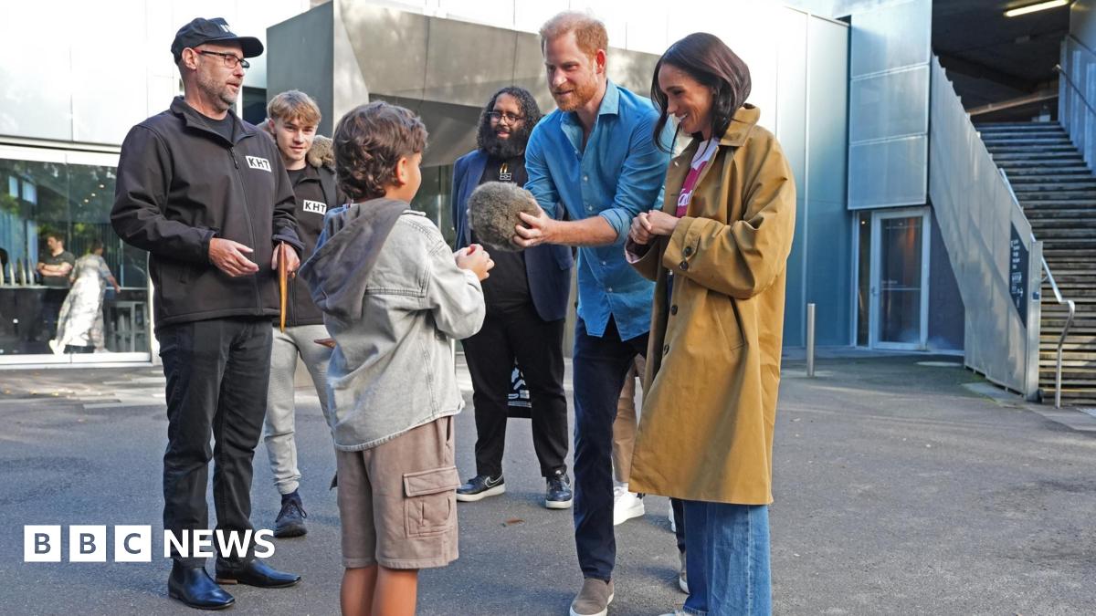 A small boy faces the Duke and Duchess of Sussex, as Prince Harry holds a fur ball and others surround them watching on.