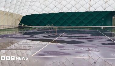 The inside of a white dome. There are tennis courts inside with nets. There are large puddles around the dome.