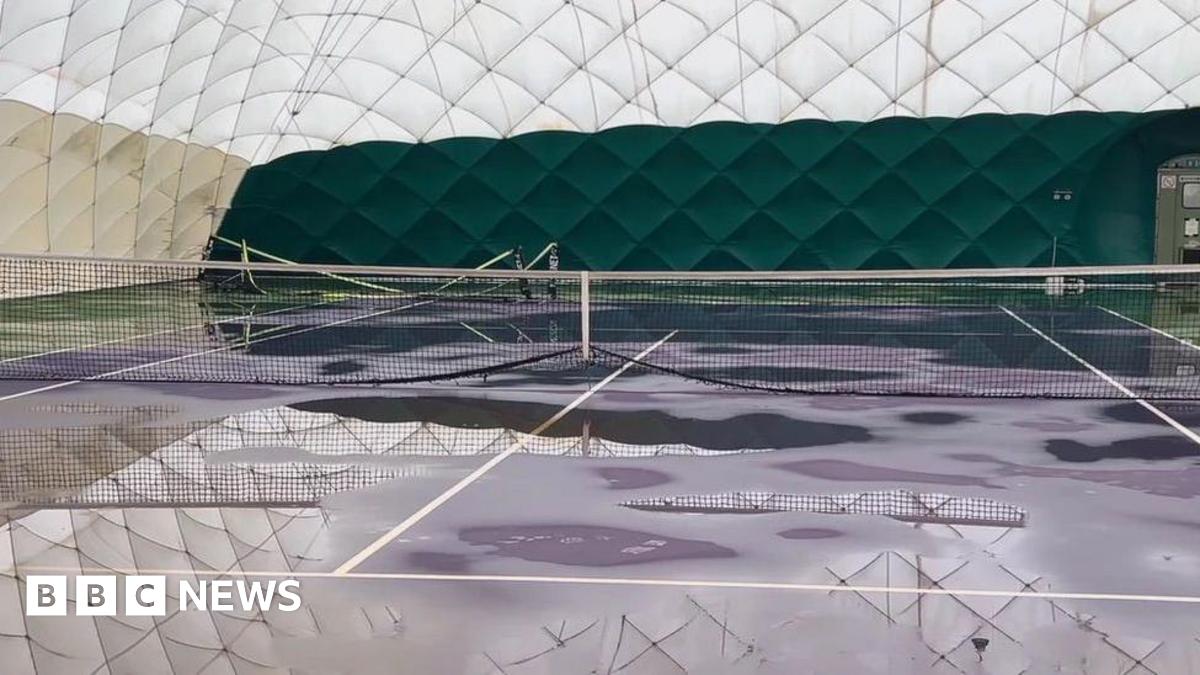The inside of a white dome. There are tennis courts inside with nets. There are large puddles around the dome.