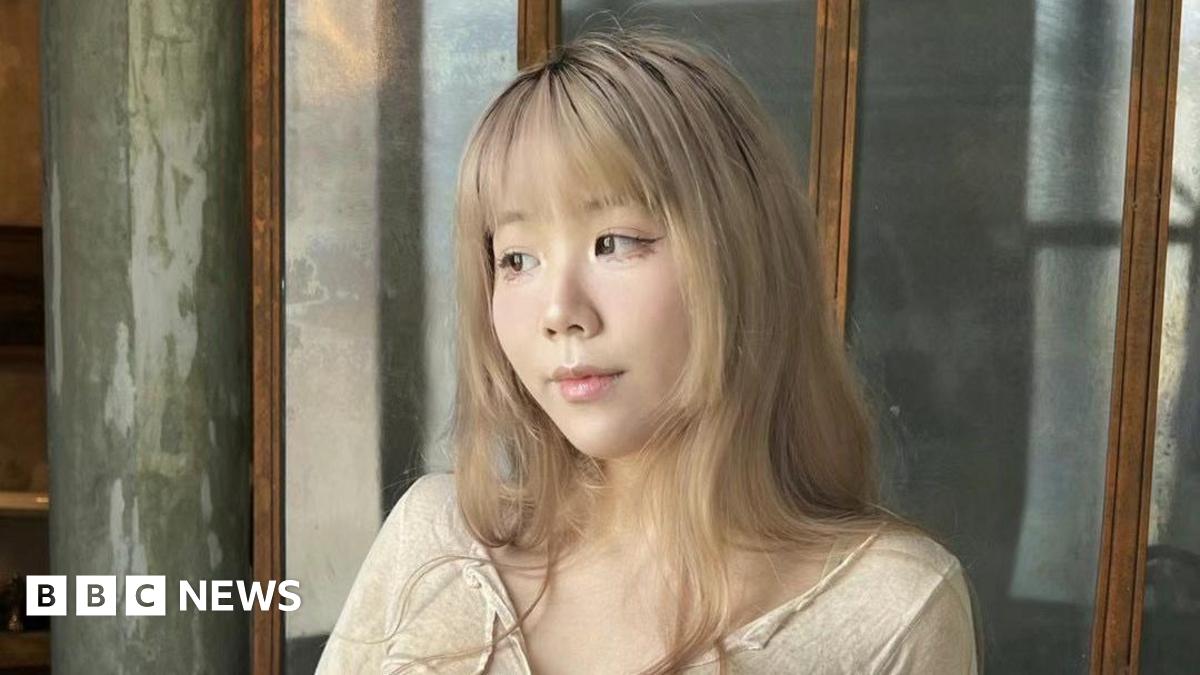 A woman with mid-length blonde hair and a fringe looks to her right, wearing a beige top and winged eyeliner.