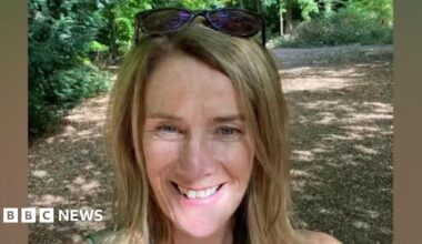 Laura Corby smiling in a selfie taken on a path through some trees on a sunny day.