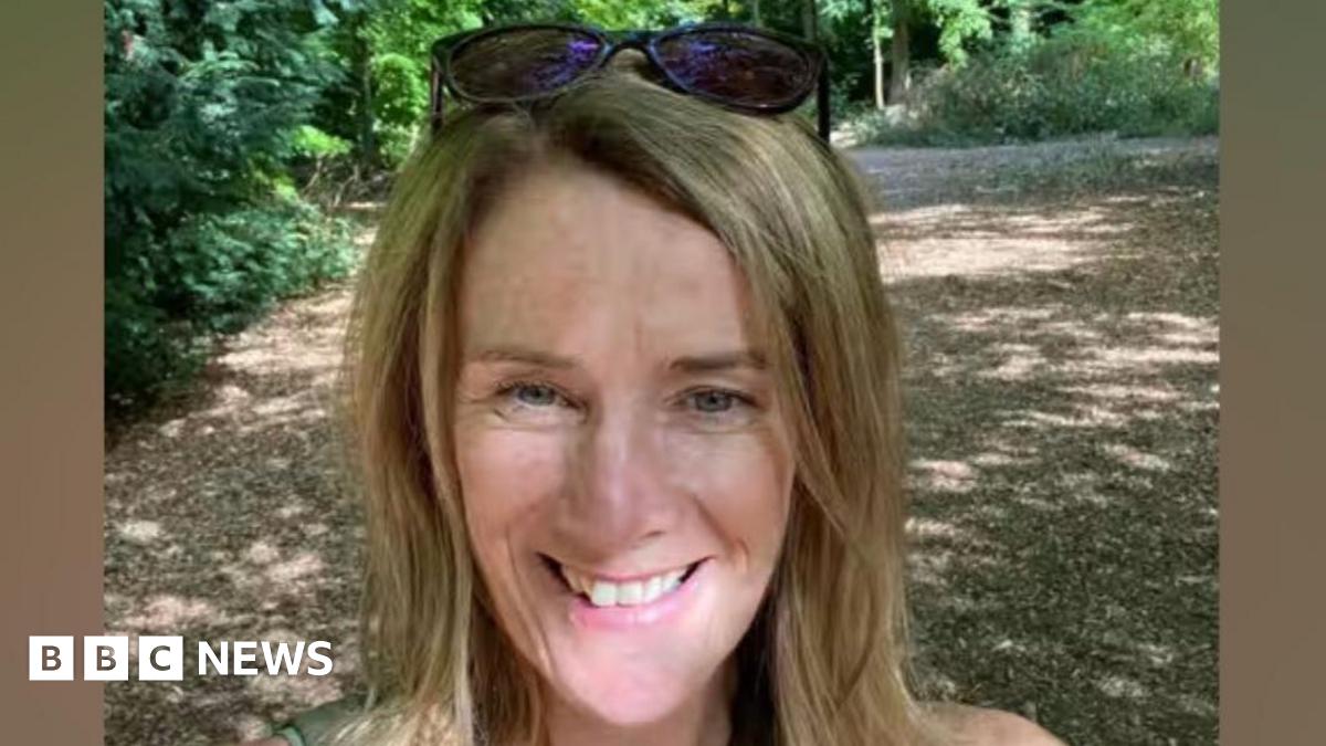 Laura Corby smiling in a selfie taken on a path through some trees on a sunny day.