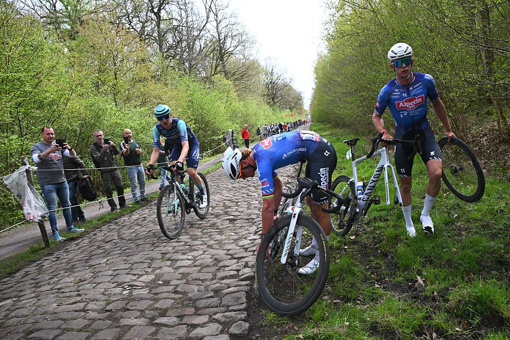 Alpecin-Premier Tech's Dutch rider Mathieu van der Poel (C) exchange his bike with Alpecin-Premier Tech's Belgian rider Jasper Philipsen (R)