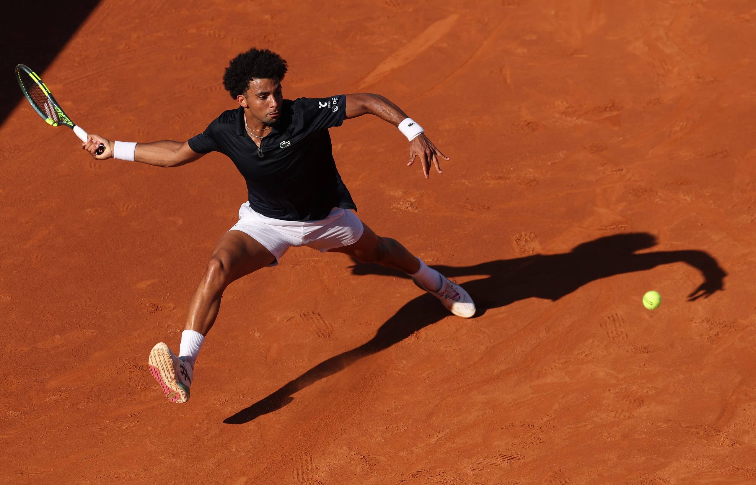 Arthur Fils prepares to hit a forehand on the run on a clay tennis court.