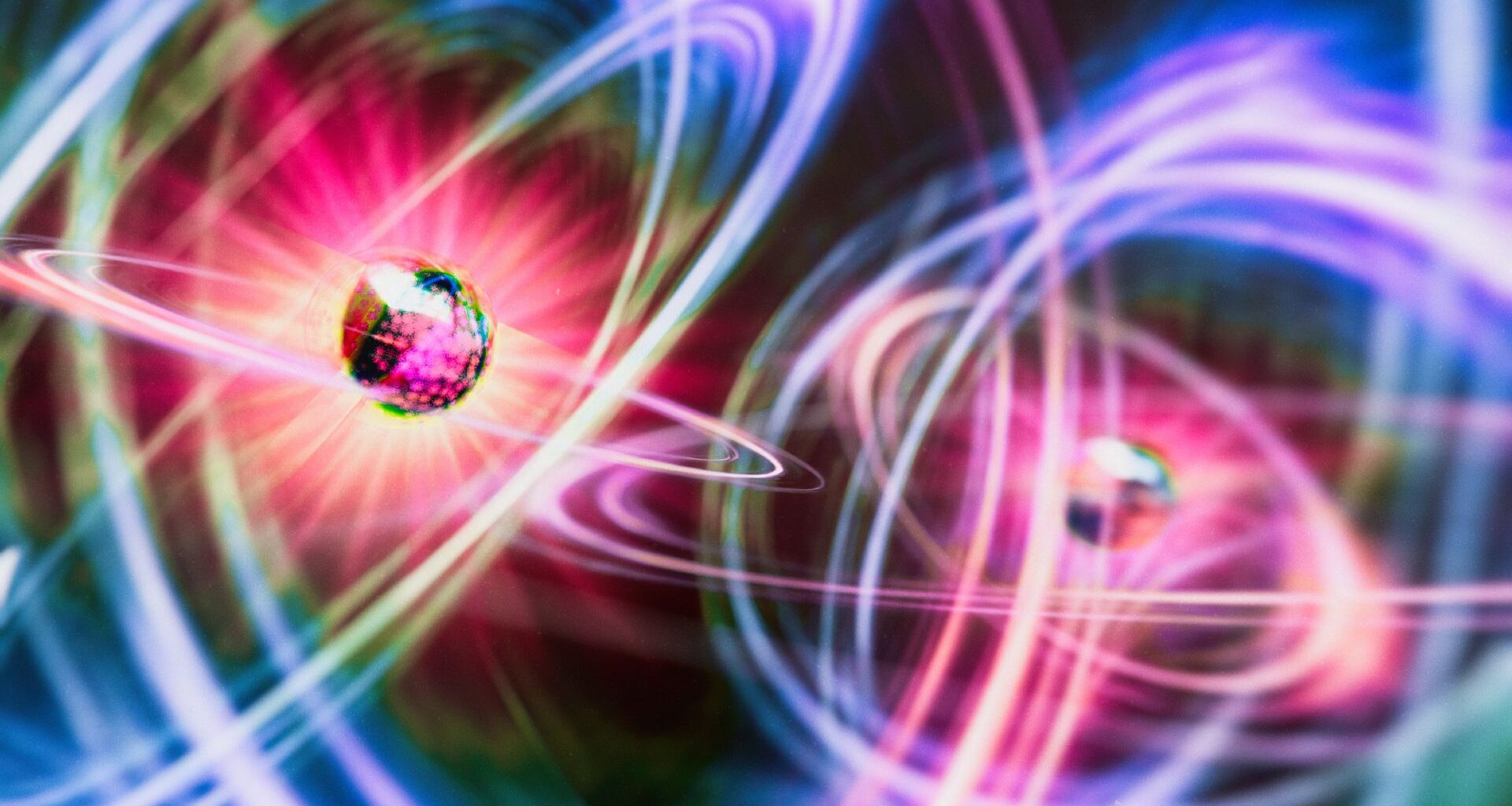 An illustration of two particles as glowing geodesic shapes surrounded be halos of pink, yellow and blue light