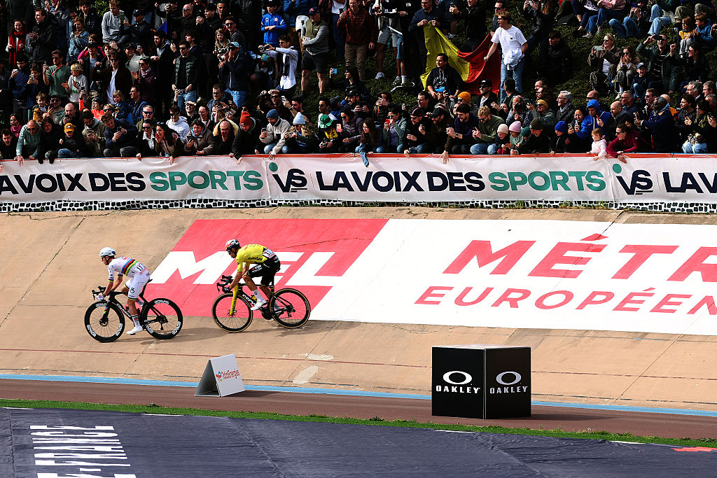 Tadej Pogačar and Wout van Aert ride on the velodrome in Paris-Roubaix, with huge crowds lining the bankings of the track