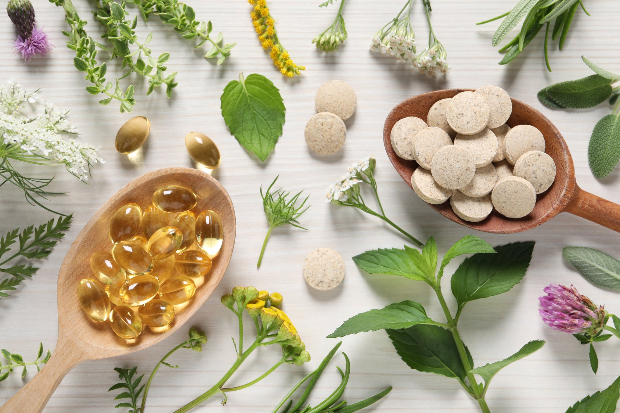 Different pills, herbs and flowers on white wooden table, flat lay. Dietary supplements