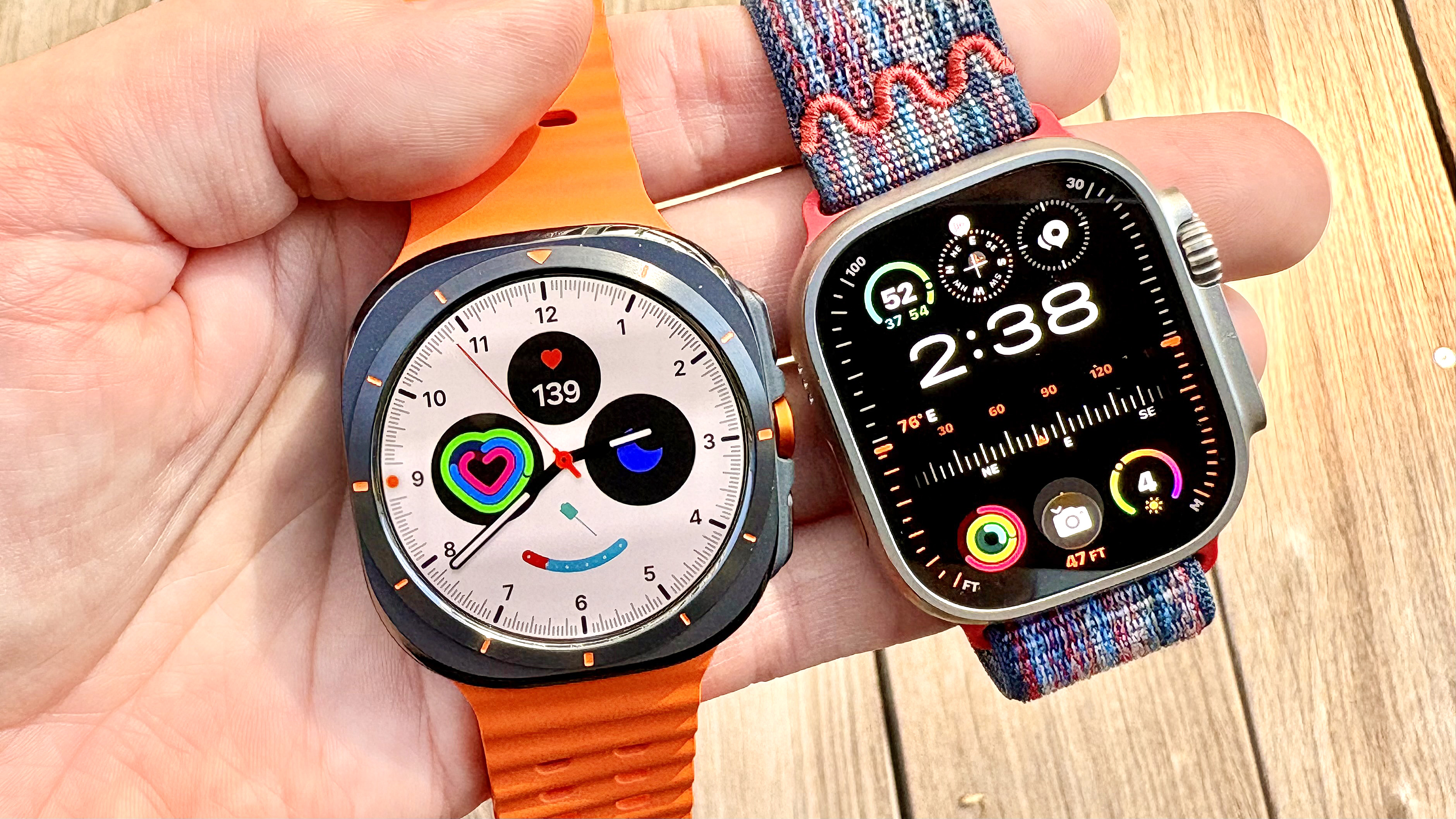 Close-up of the Apple Watch Ultra 3 next to the Samsung Galaxy Watch Ultra in the writer's hand against a colorful background