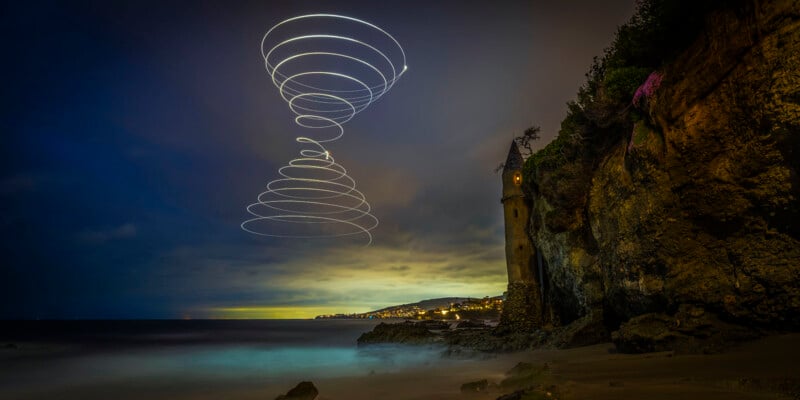 A spiral trail of lights swirls above a coastal scene at dusk, featuring a tall, narrow stone tower by rocky cliffs and a misty shoreline, with a distant town illuminated under a moody sky.