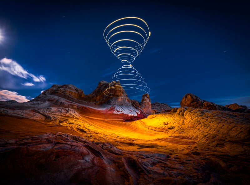 Alien desert landscape at night with rocky, layered hills, illuminated in orange and yellow hues, and swirling spiral light trails rising into the dark blue sky.