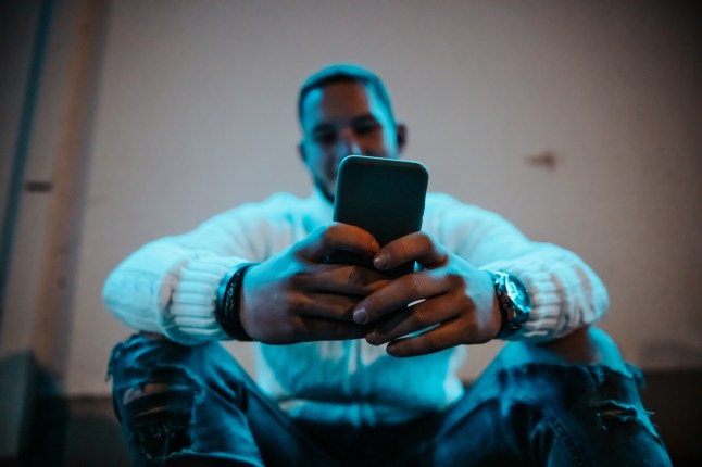 Young man checking news and posts on mobile phone in the city at night