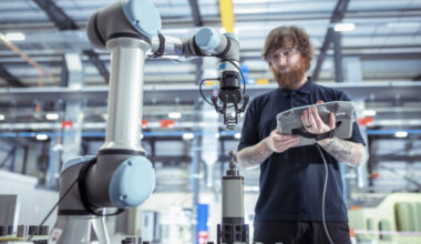 Image of a man with a computer tablet standing in front of an industrial robotic arm.