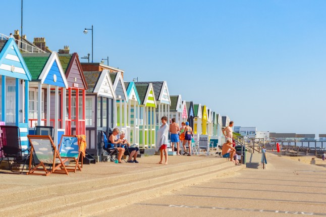 People enjoying the sunshine on the promenade of Southwold beach lined with a row of beach huts